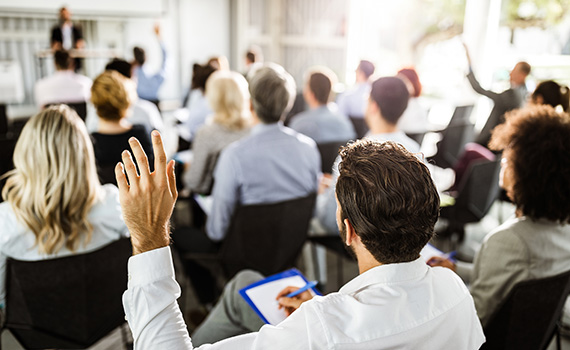 Back view of a businessman raising his hand at a seminar as he takes notes