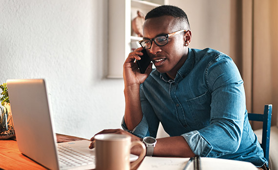 Young male on his phone and using his laptop, he is sitting down at home