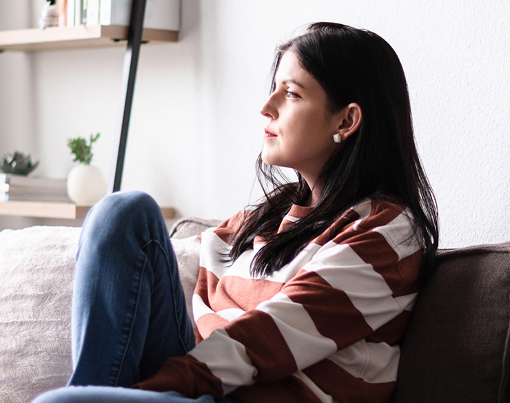 A sad woman sitting on a couch and looking outside