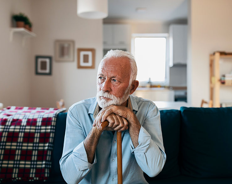 An elderly male holding a cane, he is sitting and looking to the side